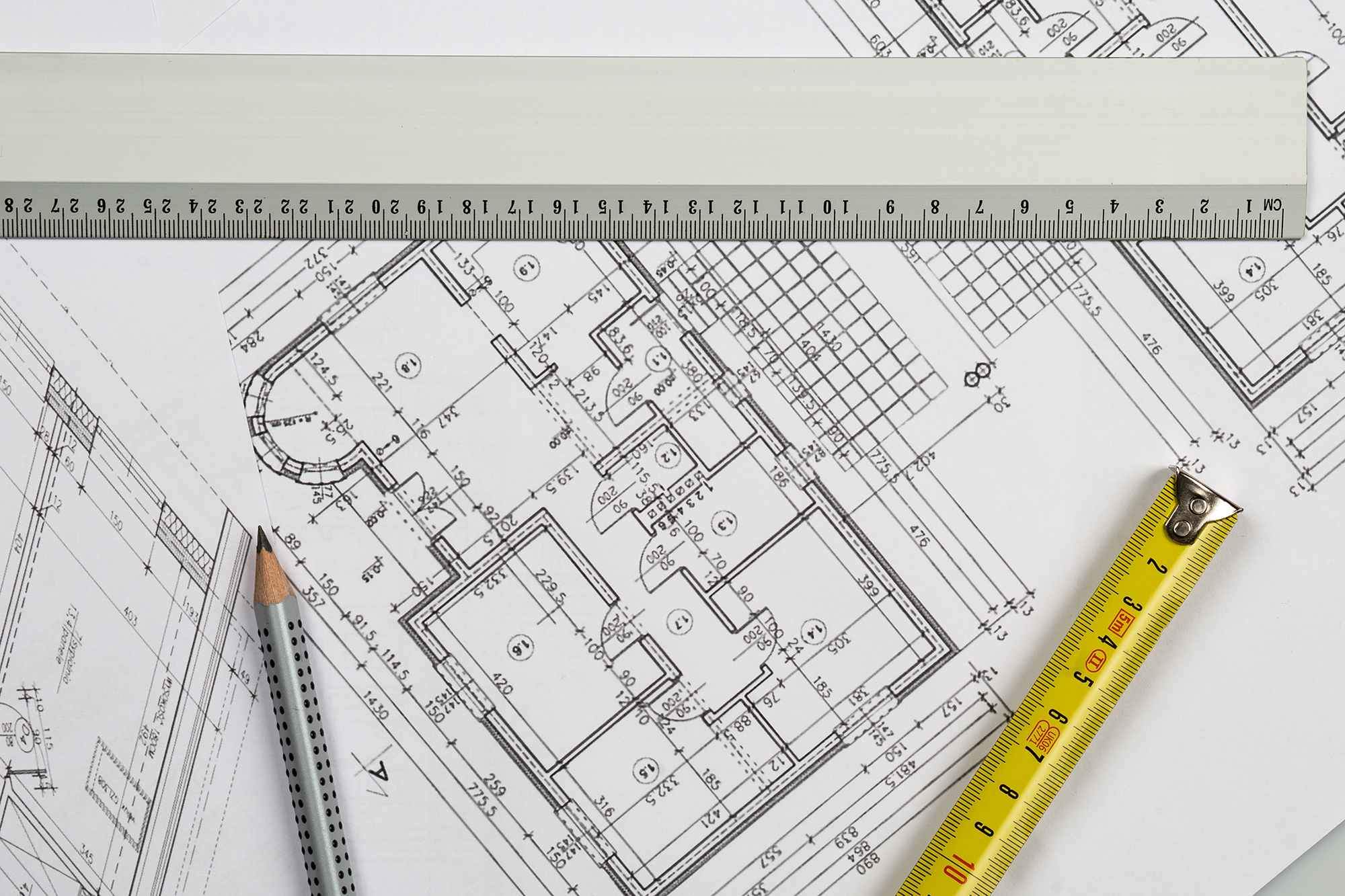 Laying beside the architectural floor plans showcasing room layouts and precise dimensions are a pencil, ruler, and a yellow measuring tape. This meticulous design work reflects the expertise of Cory Maurer, akin to crafting an employee profile with precision and attention to detail.