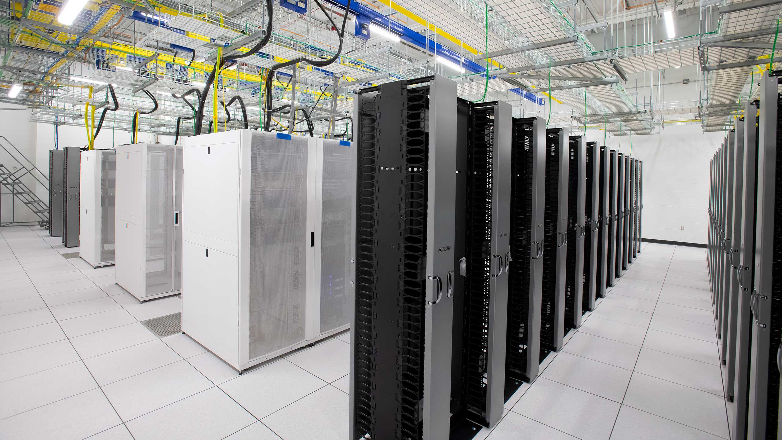 A modern municipal data center interior with rows of black and white server racks. The ceiling is equipped with cable trays and cooling ducts. The room is brightly lit and has a tiled floor, conveying a clean and organized environment.