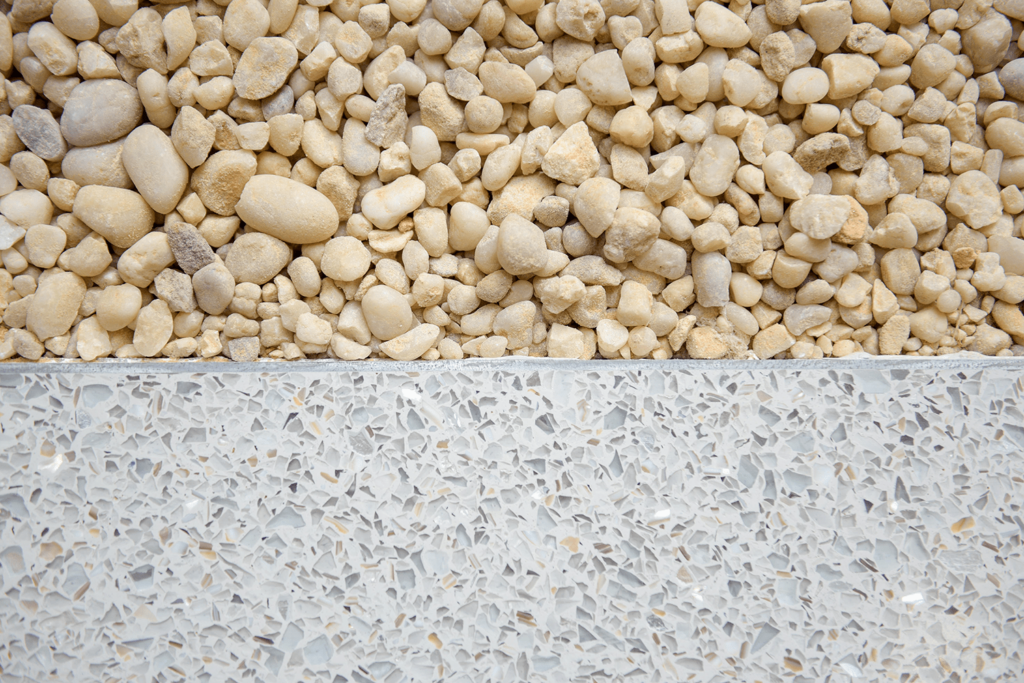 Close-up of small beige pebbles on textured gray terrazzo flooring, reminiscent of a modern hospitals serene design. The contrasting textures and colors offer a tranquil aesthetic, akin to the peaceful atmosphere found in St. Mary Mercys worship space.